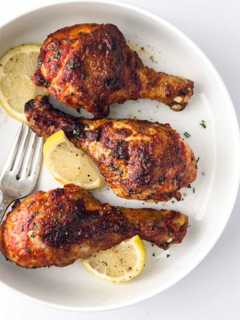 Cooked tandoori chicken leges on white plate with lemon slices and fork. 