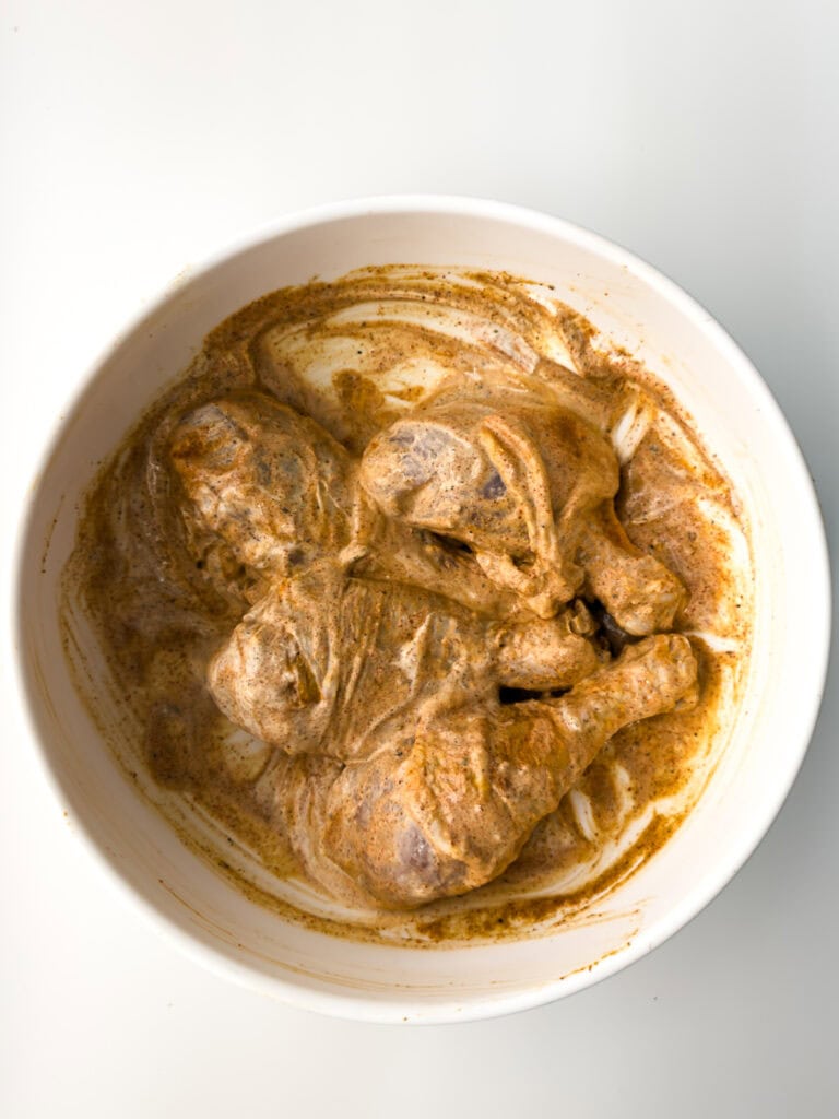 Chicken legs in yogurt marinade in white bowl