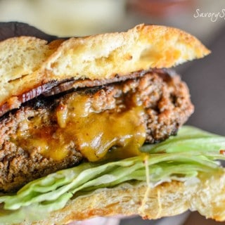 Holding one of the Cheese Stuffed Chorizo Burgers in the left hand and showing the juicy burger in-between the buns